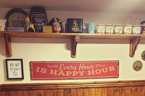 Tiny-Taven-4 Every hour is happy hour sign below a shelf of bar memorabilia